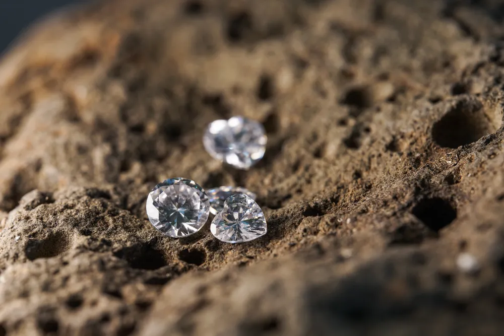 Drei funkelnde 3-Karat-Diamanten liegen auf einer strukturierten Natursteinoberfläche und reflektieren das Licht in perfektem Glanz