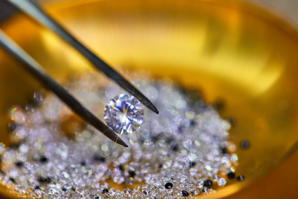 Makelloser FL Diamant wird mit Pinzette über einer goldfarbenen Schale mit kleinen Diamanten gehalten