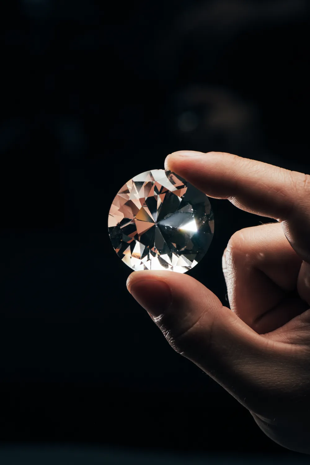 Person hält einen großen, klar geschliffenen VS1 Diamanten zwischen den Fingern, Nahaufnahme mit Lichtreflexen